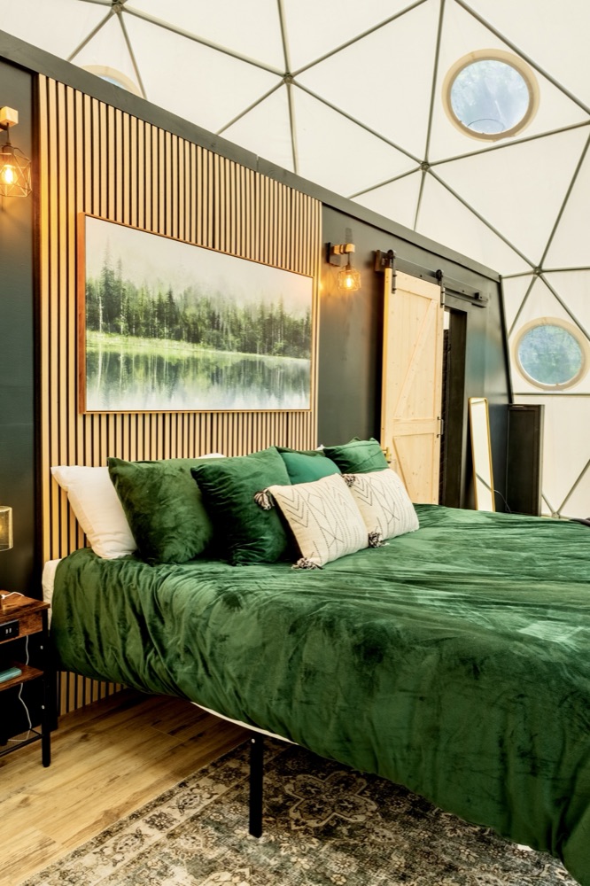 Geodesic dome bedroom with forest-green velvet bedding and wood-slat accent wall